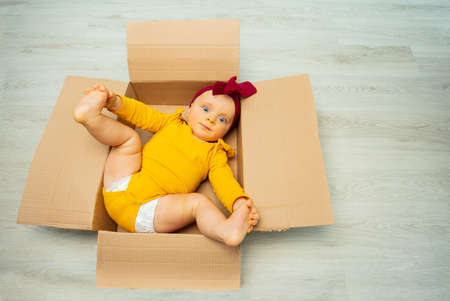 Baby girl in open cardboard box on the floorの写真素材