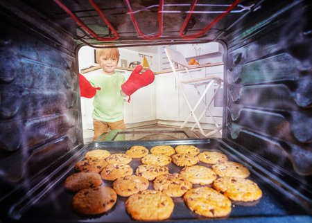 Blond boy with oven-gloves check cookies in ovenの写真素材