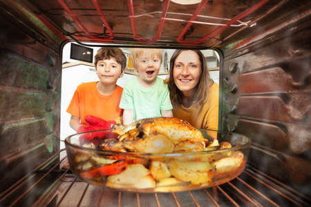 Mother and two boys take roasted chicken from ovenの写真素材