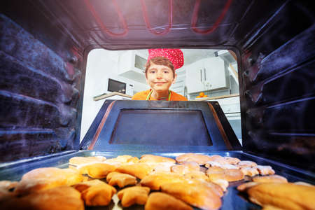 Happy laughing boy open oven door to take cookiesの写真素材