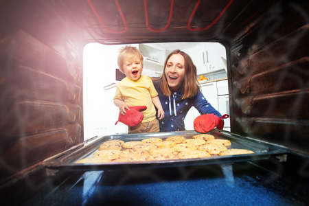 Mother and son take cookies out of oven together
