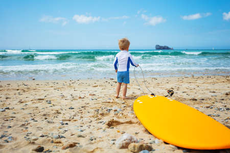 Little boy stand with surfboard looking sea wavesの写真素材
