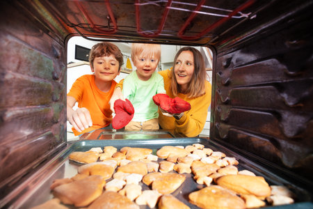 Mother and boys smile take cookies tray from ovenの写真素材