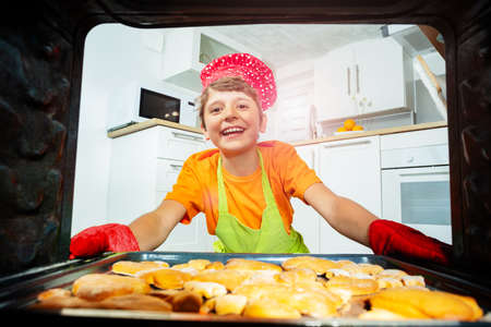 Happy laughing boy take baked cookies from ovenの写真素材