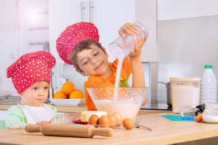 Boys cooking in chef hat add sugar to mixing bowlの写真素材