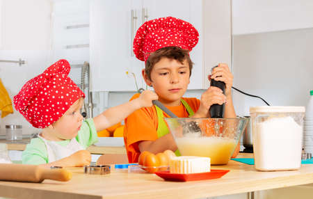 Two happy boys mix dough in bowl preparing cookieの写真素材