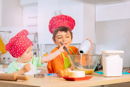 Boy pour out milk to the bowl preparing doughの写真素材