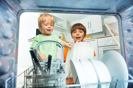 Two boys take dishes from dishwasher at kitchenの写真素材
