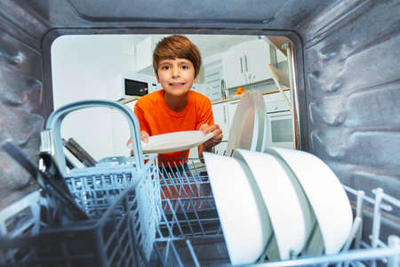 Boy smiling take plates from dishwashing machineの写真素材