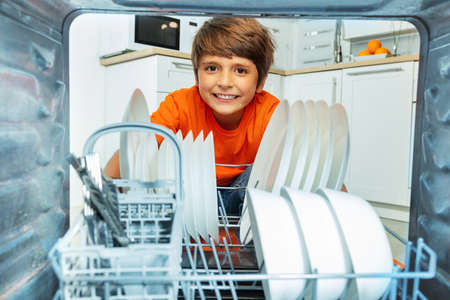 Boy smiling take plates from dishwashing machineの写真素材