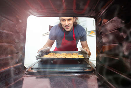 Man take a tray with cookies from oven inside viewの写真素材