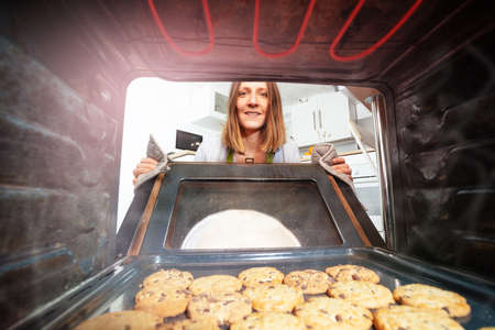 Woman open door to oven with freshly baked cookiesの写真素材