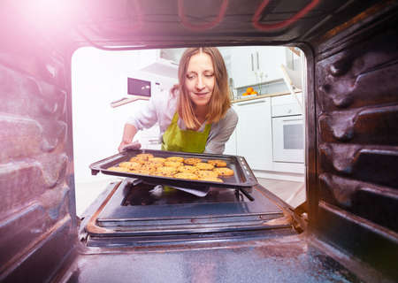 Woman take tray with cookies from oven inside viewの写真素材