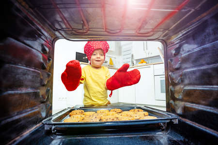 Boy with oven-gloves take cookies tray from ovenの写真素材