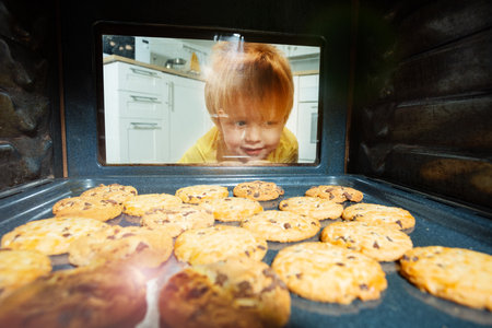 Curious boy look though oven glass at cookiesの写真素材