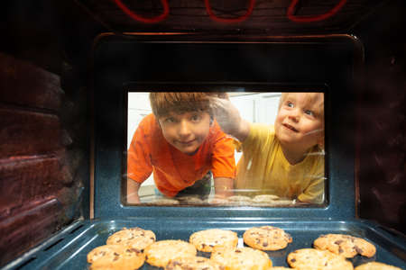 Boys brothers look though oven glass at cookiesの写真素材