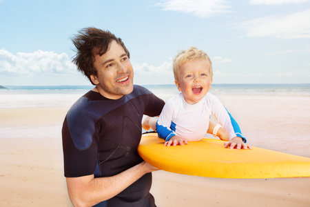 Father carry son play with surfboard on the beachの写真素材