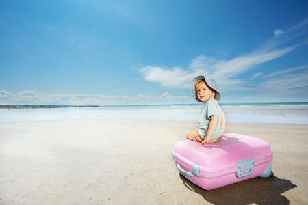 Vacation concept a boy sit on suite case at beachの写真素材