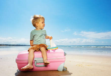 Cute sailor boy on baggage suitcase with toy boatの写真素材