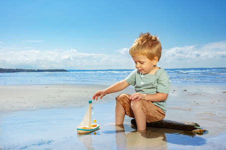 Little boy paly with toy sail ship on the beachの写真素材