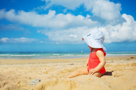 Cute baby girl in red swimsuit sit on sand beachの写真素材
