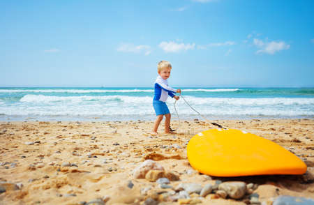 Little toddler pull surfboard to the sea wavesの写真素材
