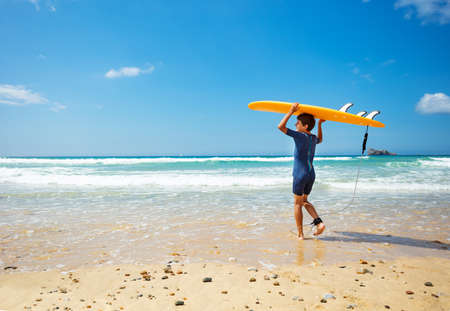 View from behind of a boy enter sea with surfboardの写真素材