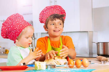 Two boys crumble dough with hands in chef hatsの写真素材