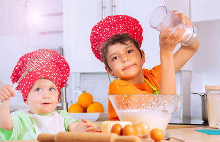 Boy add sugar to mix bowl make dough with brotherの写真素材