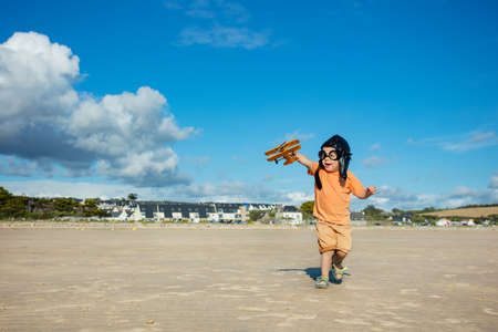 Boy with toy plane in aviation hat run on beachの写真素材