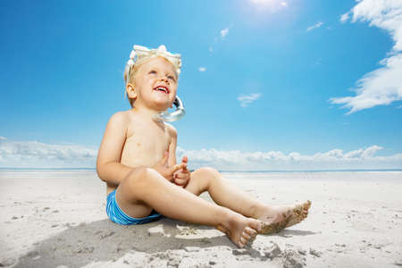 Little boy sit on sea beach with snorkeling maskの写真素材