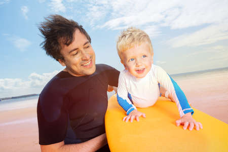 Father and son play with surfboard on the beach