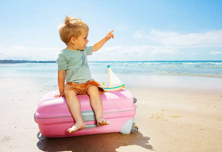 Boy play sit on a vacations suitcase at sea beachの写真素材
