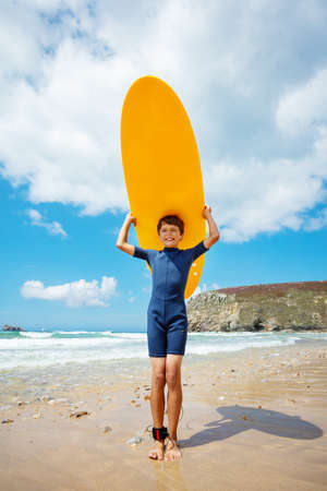 Cute boy stand holding orange surfboard over headの写真素材