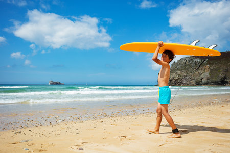 Boy walk into the sea holding surfboard over headの写真素材