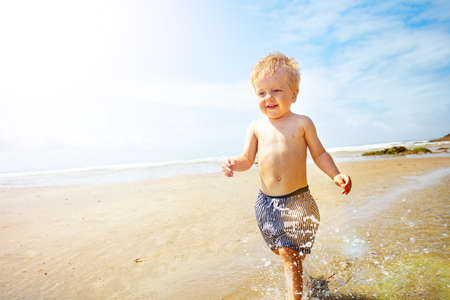 Child boy run fast and splash on a sand sea beachの写真素材