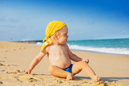 Toddler boy in bandana on sand beach look at seaの写真素材