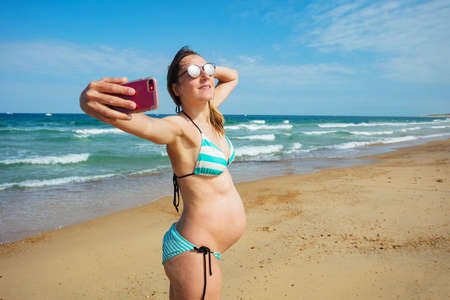 Pregnant woman on vacations take selfie at beachの写真素材
