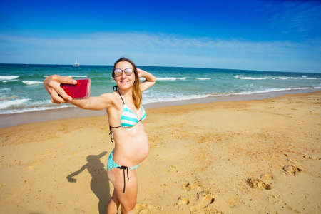 Pregnant woman on sea beach make selfie with phoneの写真素材