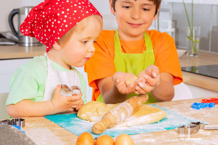 Two kids roll dough and cut shapes on the kitchenの写真素材