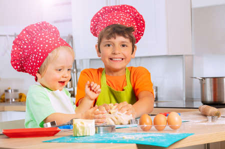 Two kids crumble dough with hands in chef hatsの写真素材