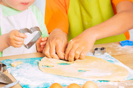 Child hands cutting out cookies in heart of doughの写真素材