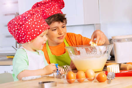 Boys add eggs and butter to mixing bowl cookingの写真素材