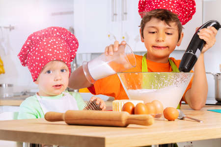 Boy add sugar and mix dough in bowl with brotherの写真素材