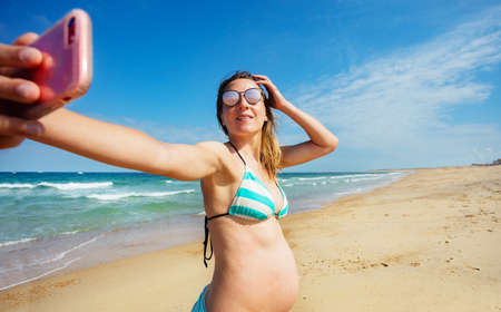 Pregnant woman take photo of her on sea beachの写真素材