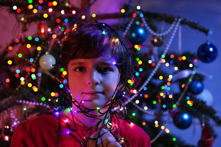 Boy face with garland lights by Christmas treeの写真素材