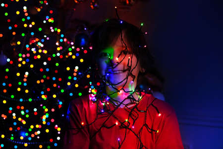 Christmas spirit: boy with garland lights on faceの写真素材
