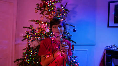 Boy at home by Christmas tree hold garland lightsの写真素材