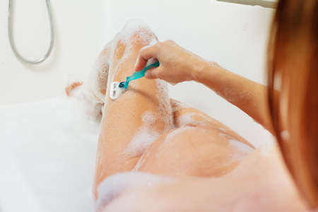 Pregnant woman shave leg sitting in bath with foamの写真素材