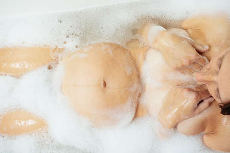 Pregnant woman in bath with foam close-up of bellyの写真素材